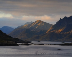 The photo captures the mood of one of the fjords of Lofoten, in the moment when rays penetrate through the lead rainy sky and enlightened mountain slopes.